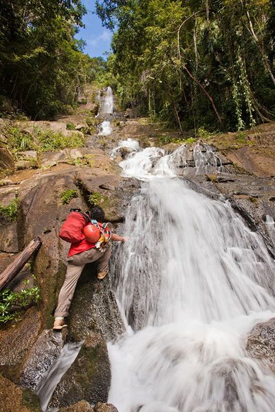 man with climbing gear scaling a tall waterfall