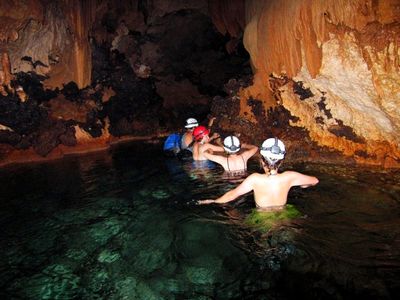 people in waist deep water with helmets exploring cave