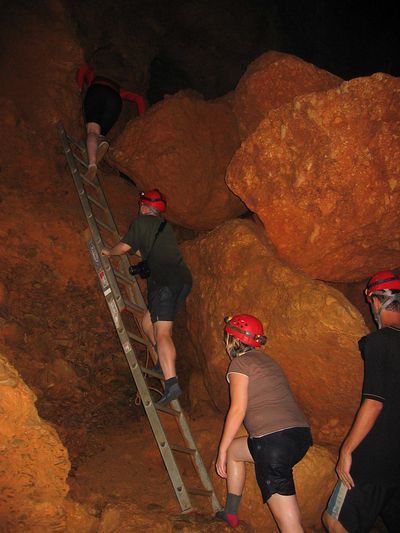 people with red helmets climbing ladder in a cave