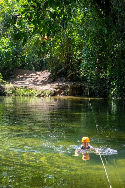 woman with helmet crossing river while grabbing to rope