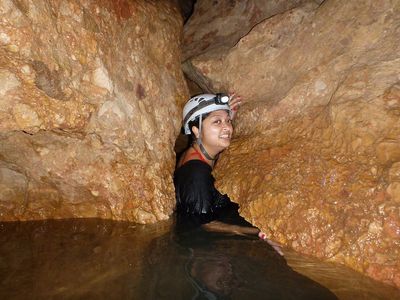 woman with white helmet squeezing through cracks in a cave