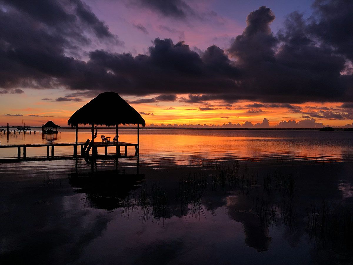 silhouette of thatch house and sunset by lagoon