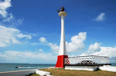 lighthouse with red base and boat passing in background