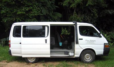 white shuttle van with rainforest in background