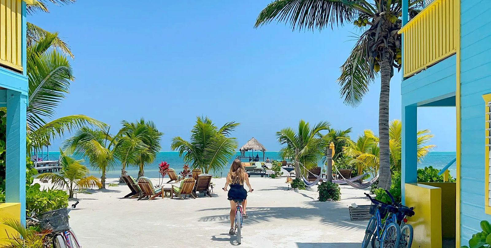 woman biking to beach with small pal trees and hammocks