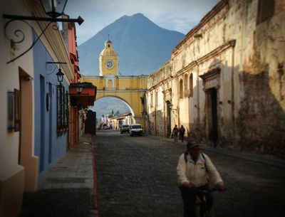 clock building with volcano in backgorund and man passing in the foreground