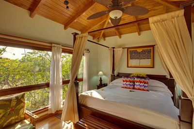 queen bed in high ceiling room with wooden ceiling fan and jungle view