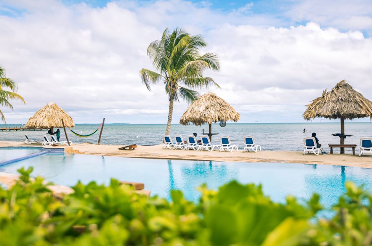 pool in front of beach with thatch rooftops and beach chairs