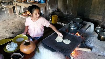 young girl preparing tortillas on a comal in mayan kitchen