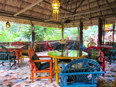 thatched roof open restaurant with tables and colorful chairs under it