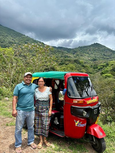 Maria and her husband and his tuk tuk man and woman beside small red tuk tuk