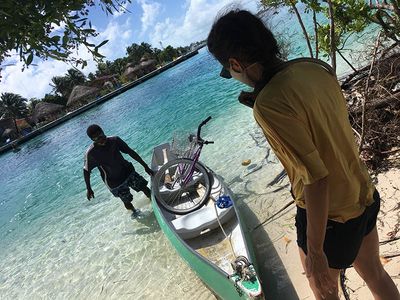 man bringing bike in canoe to caye