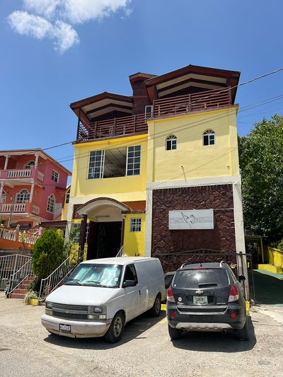 Yellow Belly Backpackers parking lot tall yellow building with two cars in front of parking lot